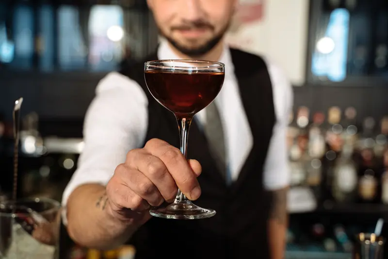Close-up of a bartender handing a cocktail in a bar. Focus on glass, perfect for lifestyle and hospitality themes