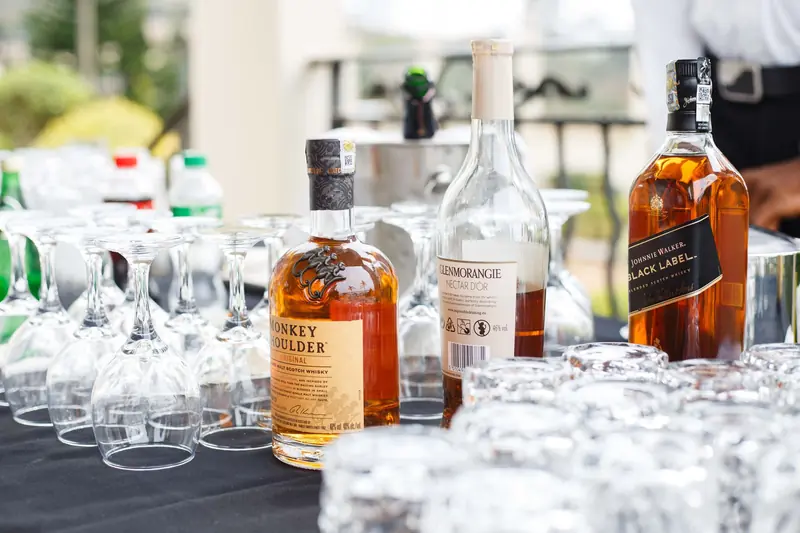 A selection of whiskey bottles arranged with empty glasses on a black tablecloth outdoors. Ideal for parties