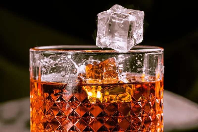 A detailed shot of whisky in a patterned glass with an ice cube mid-air, evoking elegance
