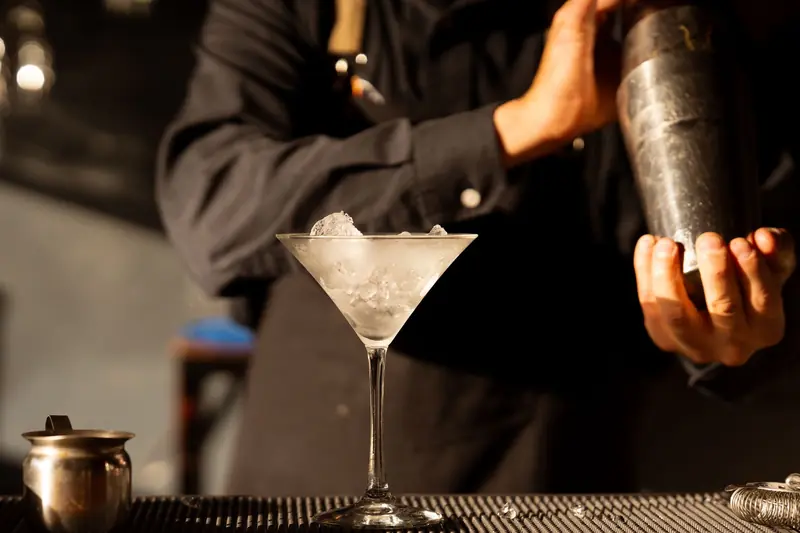 A bartender making a cocktail with a shaker and a glass full of ice on the bar counter