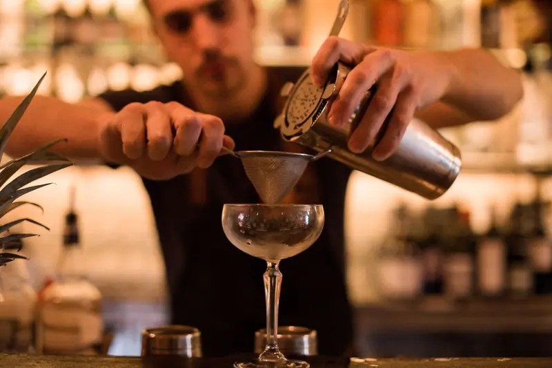 Bartender using a shaker and strainer to craft a cocktail at a dimly lit bar