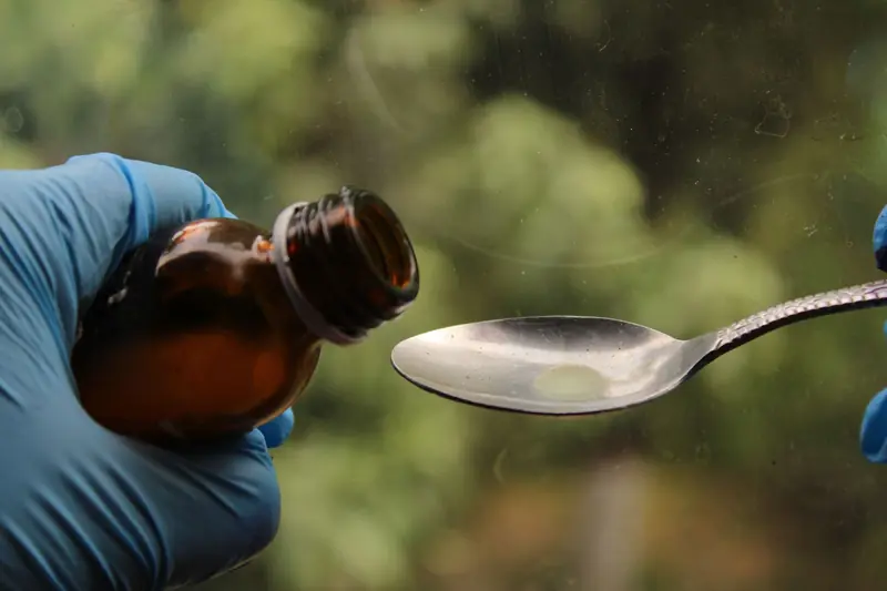Close-up of syrup being poured from a bottle into a spoon by gloved hands, medical concept