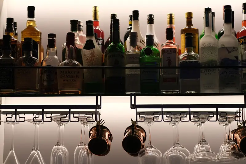 A stylish and organized display of assorted liquor bottles on a bar shelf with hanging glassware below