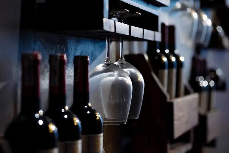 Close-up of wine bottles and glasses on wooden shelves in a dimly lit cellar, creating a cozy ambiance