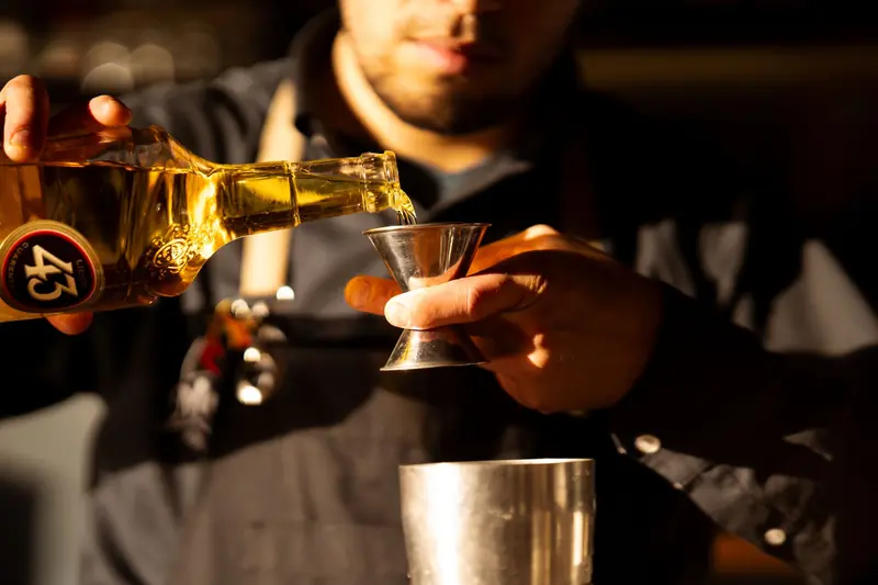 Bartender carefully measuring liquor with a jigger in warm bar setting