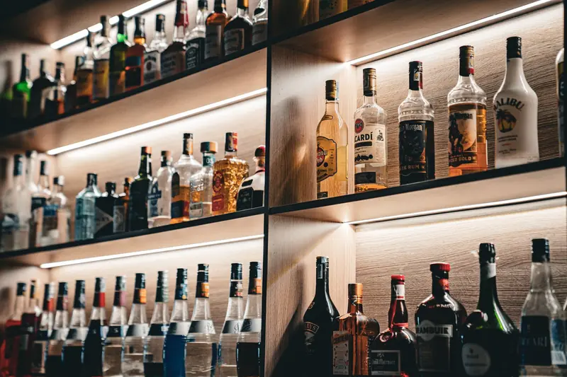 Assorted liquor bottles on a bar shelf, lit with warm ambient lighting, capturing nightlife vibes