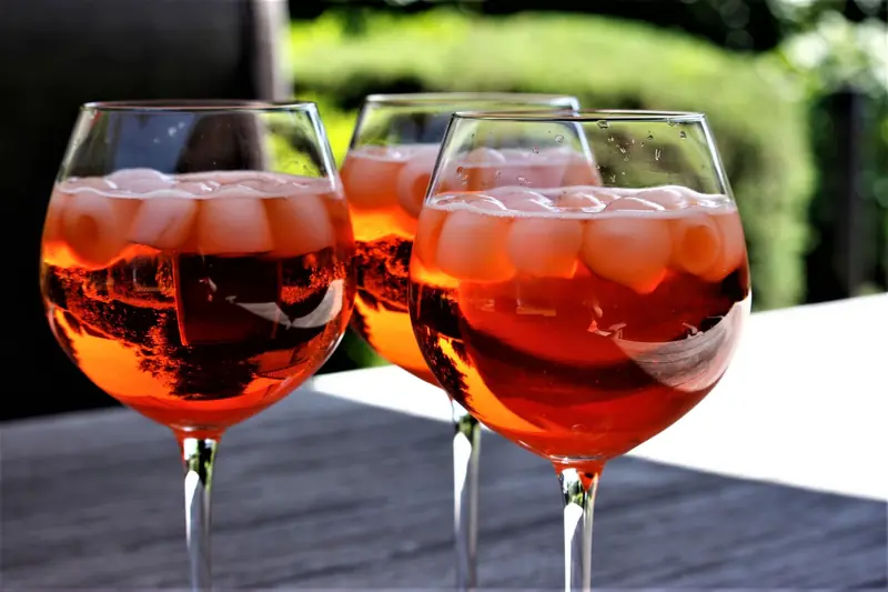 Three chilled cocktail glasses filled with a vibrant orange drink and ice cubes on a sunny day