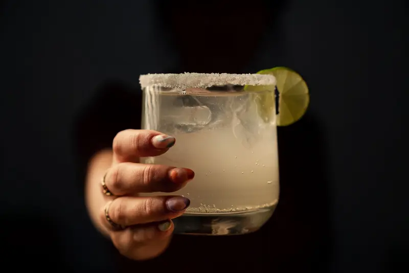 Close-up of a hand holding a margarita with lime and salt rim, perfect cocktail image